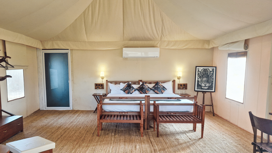 Spacious interior of a luxury tent bedroom featuring a large bed, wooden furniture, and air-conditioning - Umaria Safari Camp