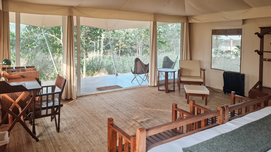 Interior view of a tent bedroom showcasing a wooden bed frame and large glass doors opening to the outdoors - Umaria Safari Camp