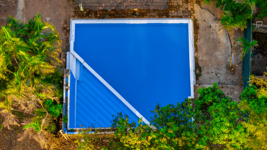 Top aerial view of the swimming pool at Nature Trails Durshet surrounded by dense greenery, palm trees, and natural landscapes.