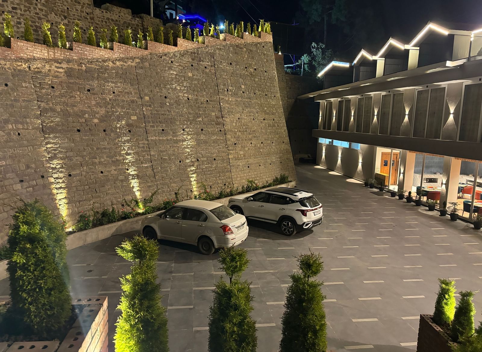 Well-lit outdoor parking area with stone wall and multiple cars parked – ARNISA Boutique Hotel