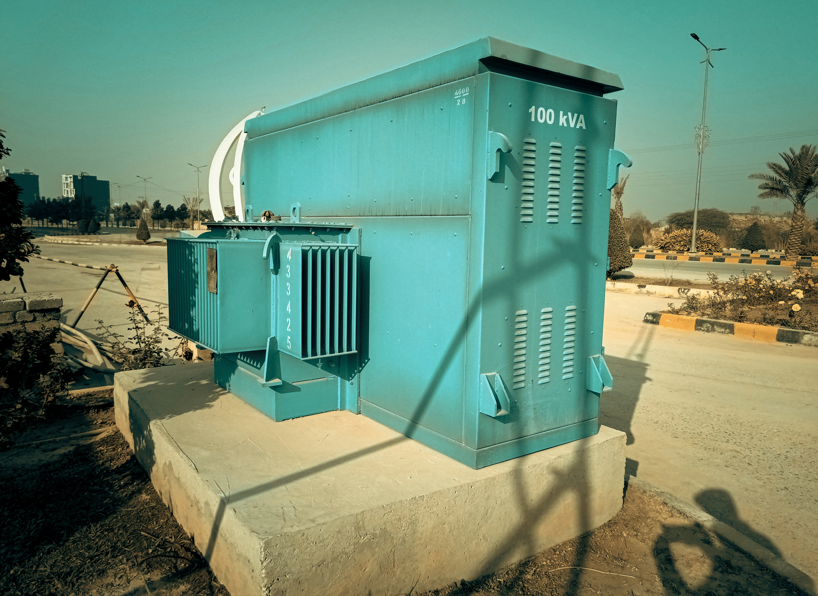 An outdoor electrical generator, mounted on a concrete slab near a road.