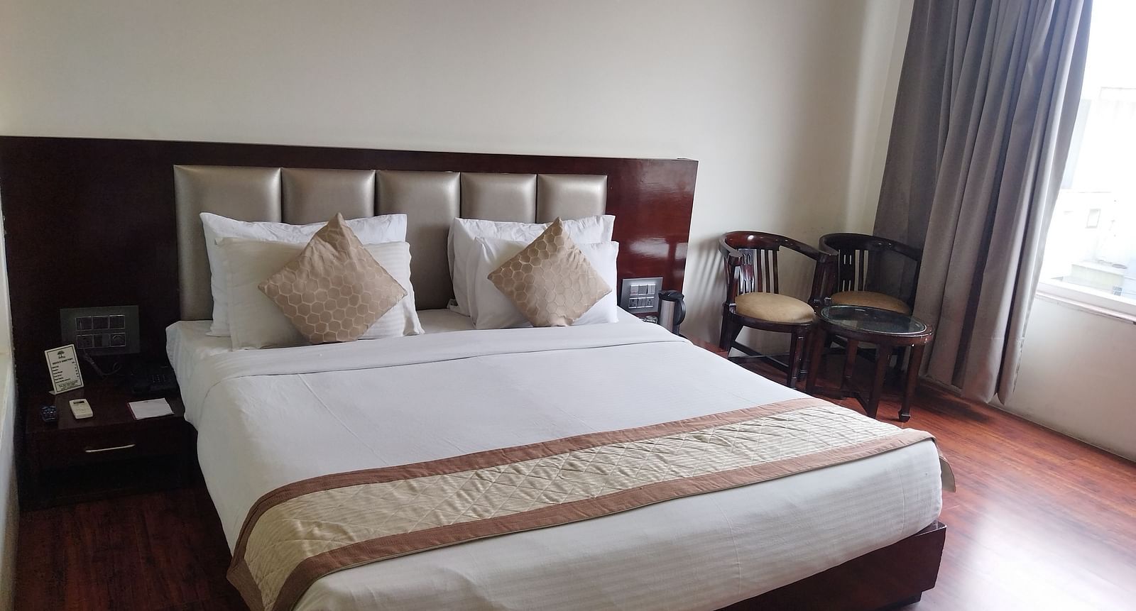 A hotel room with a large bed draped in beige and brown linens and furniture to relax - TGI Apple Inn, Jaipur 