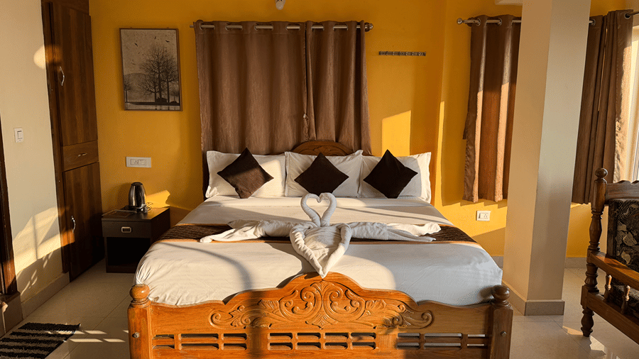 A bedroom with yellow walls featuring a wooden double bed with white linen and towels folded into a heart shape | Kollanoor Guest House, Coorg