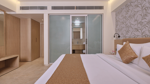 A bedroom with a built-in wooden wardrobe, luggage rack, and bathroom doorway with the bed in the foreground at Biznotel by Pride Motera, Ahmedabad.