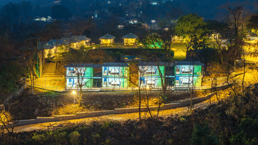 Alt Text: Aerial night view of Nature Trails Durshet resort glowing with warm lights nestled among lush hills and trees.