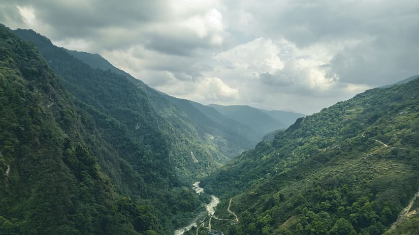 View of mountains with river flowing in between and cloudy sky in the background.