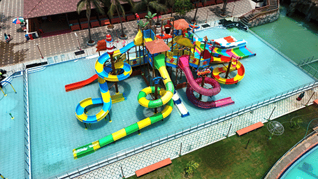 Aerial view of the Splash Zone play structure with yellow, green, purple and red slides in a shallow pool, lined with palm trees at MGM Dizzee World, Chennai.