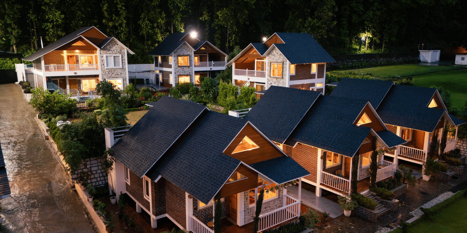 A evening view of cottages warmly lit amidst lush green surroundings - Megha Resort & Villas, Dehradun
