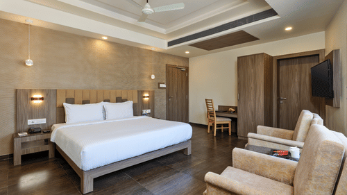 Premium Room at Pride Biznotel Sasan Gir featurinfg a double bed with nightstands on both sides and sitting space in front of it and a work desk in the background