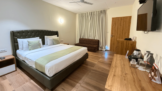 Modern cottage-style hotel room featuring a spacious bed, warm wooden accents, and a wall-mounted TV at VITS Daman Devka Beach.