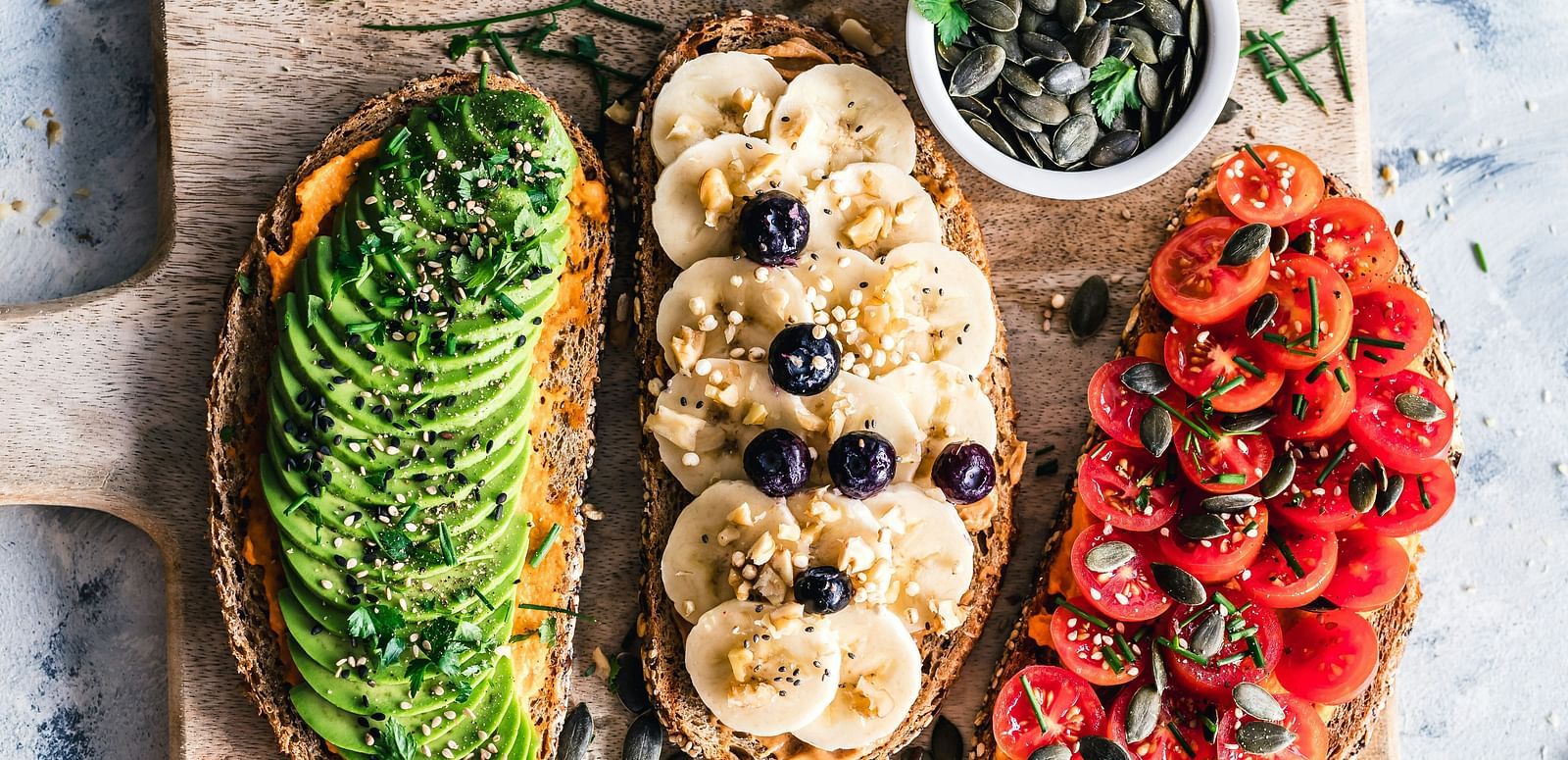 Wooden board topped with avocado toast, berry-topped pancakes, and tomato toast slices.