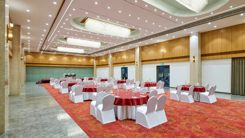 An image of a banquet hall at Tulip Inn, Bhopal, showcasing tables, chairs, and ceiling lighting.