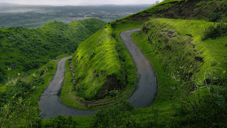 A winding tarmac road snakes through lush green hills under a moody, grey sky in the British countryside.
