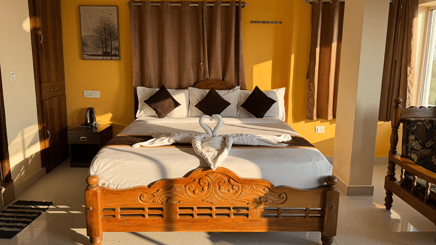 A bedroom with yellow walls featuring a wooden double bed with white linen and towels folded into a heart shape | Kollanoor Guest House, Coorg