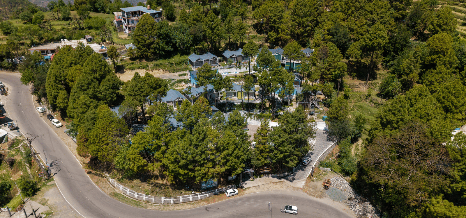 An elevated shot shows a winding road through a hilly landscape with trees and buildings - DLS Nature Trinket Resort, Dalhousie