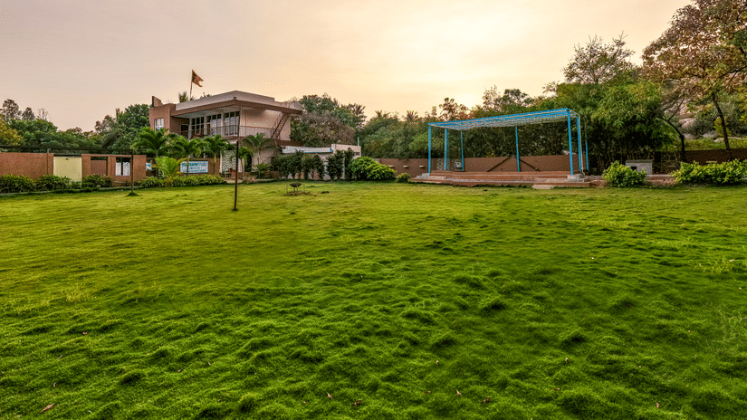 Expansive manicured green lawn at the resort during sunset, surrounded by trees - Nature Trails Ashoka Resort Hampi