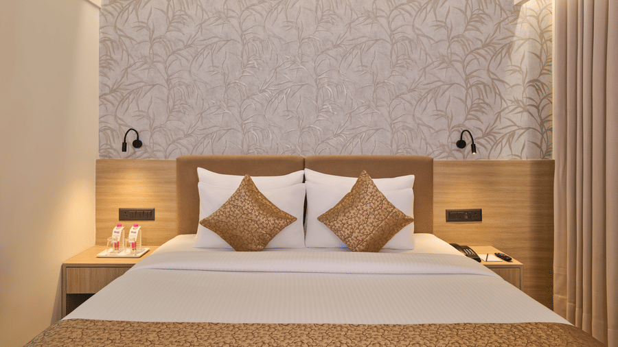 A large king size bed with patterned wallpaper, soft lighting, and gold accent pillows at Biznotel by Pride Motera, Ahmedabad.