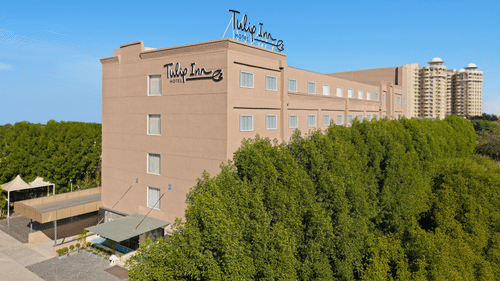 The facade of a hotel in Bhopal with trees surrounding the building - Tulip Inn, Bhopal.