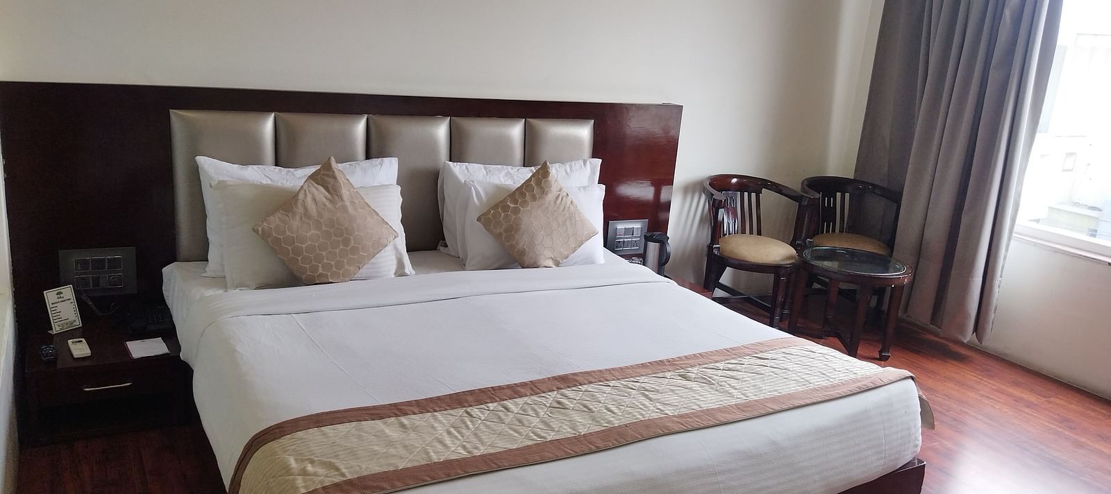 A hotel room with a large bed draped in beige and brown linens and furniture to relax - TGI Apple Inn, Jaipur 