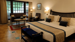 A bedroom at Jehan Numa Palace featuring a large bed with a patterned runner, warm wall-mounted lamps, and a seating area near a large window.