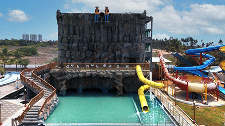 Rock-faced Thunder Falls tower with a yellow slide dropping into a turquoise pool, a wooden stairway and more slides beside it at MGM Dizzee World, Chennai.