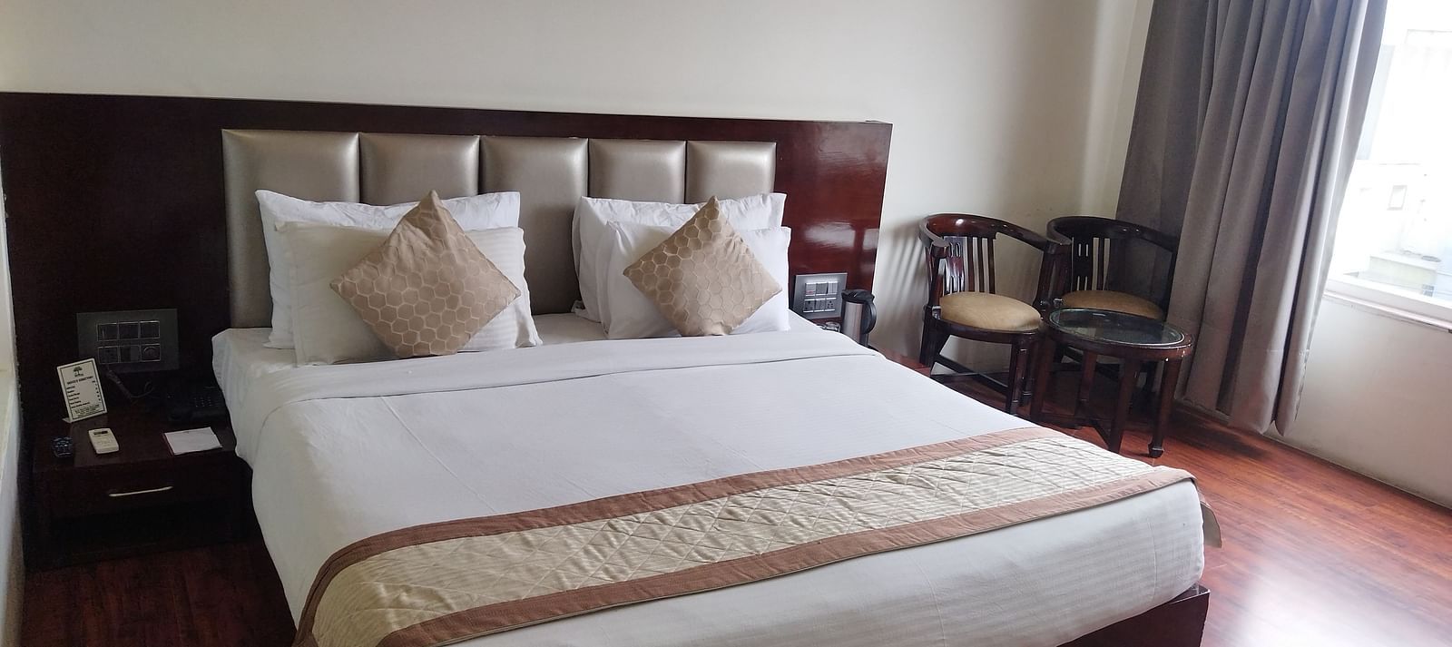 A hotel room with a large bed draped in beige and brown linens and furniture to relax - TGI Apple Inn, Jaipur 