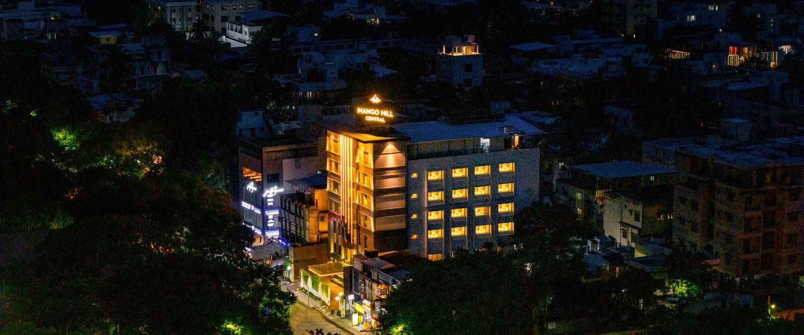 An aerial night view of Mango Hill Central, Chennai, showing the illuminated hotel building surrounded by other buildings.