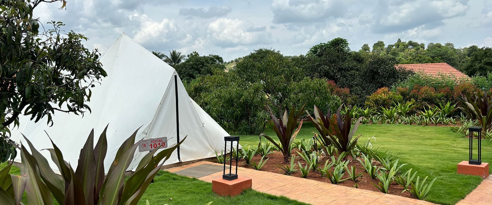 A scenic view of a resort area with tents lined along a neat walkway, surrounded by a well-maintained lawn.