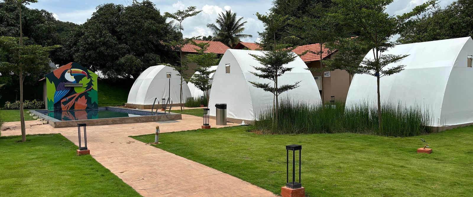 A scenic view of a resort area with tents lined along a neat walkway, surrounded by a well-maintained lawn.