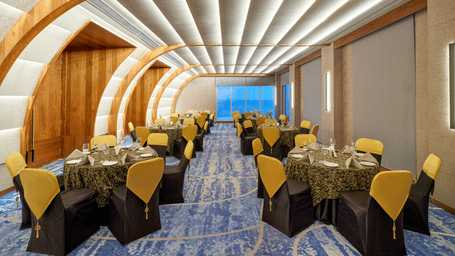 The Portrait hall at Swosti Premium Beach Resorts, Puri, with a unique curved, ribbed ceiling, set up with tables and chairs, facing the window.