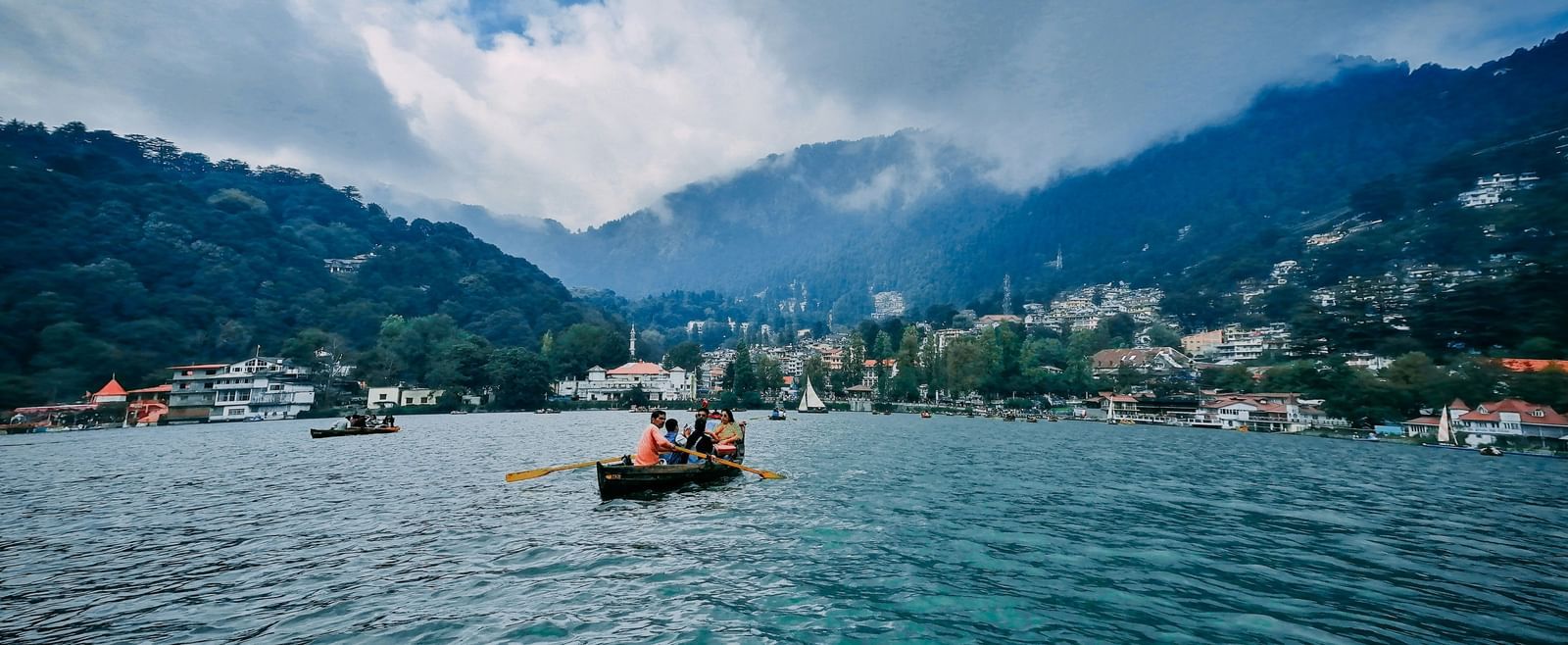 A boat sailing through a water body surrounded by lush greenery with people on board