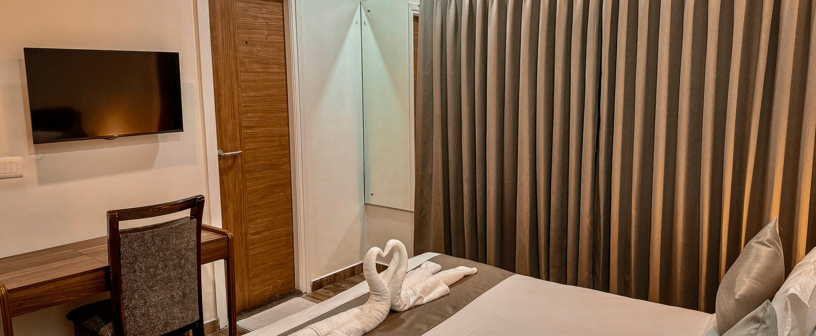 Corner view of the bedroom of Coral 4BHK featuring its queen size bed with folded towels on it, facing a wall-mounted TV | Kove Smart Stays