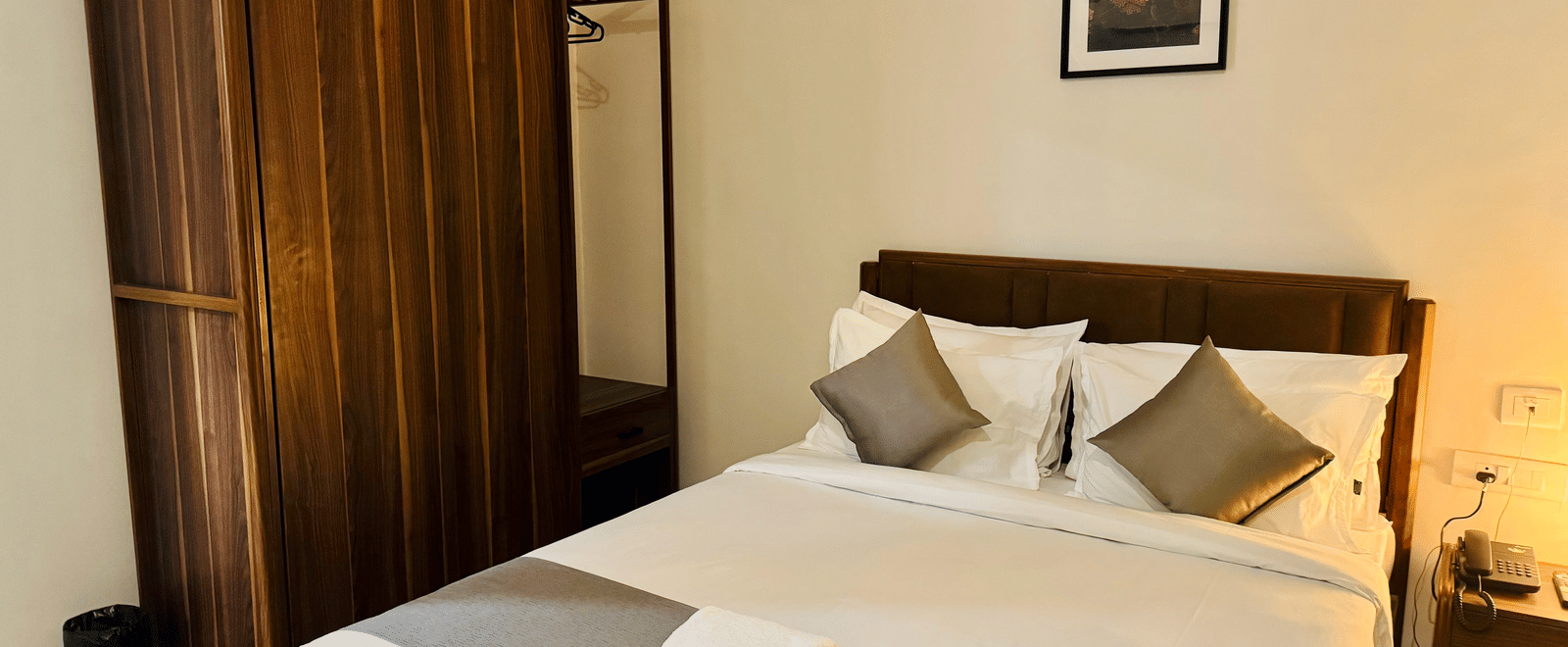 Furnishings including the queen size bed, a wooden wardrobe, and a bedside table seen in the bedroom of Coral 4BHK at Kove Smart Stays.