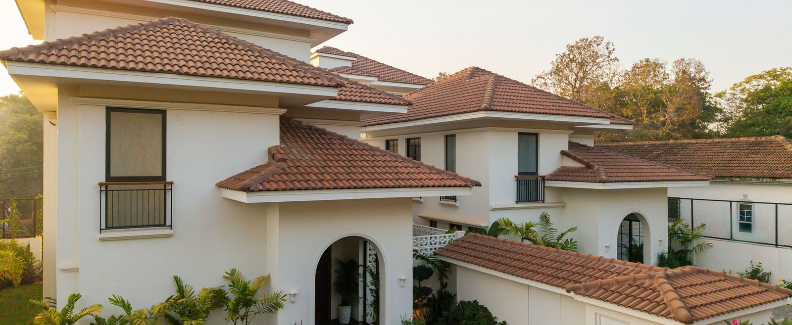 A top view of the property where the architecture is prominent along with the gate, railings, plants around the property with an impression of the sunlight and big trees visible i the background. - BluSalzz Villas - Alocassia, Anjuna