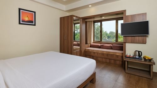 Super Desluxe Room at Pride Biznotel in Sasan Gir featuring a bed facing the TV mounted on the wall and a large window with panes made as sitting space next to it