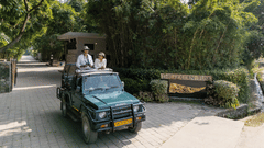 An open vehicle driving along a paved path with people seated inside and greenery on both sides.