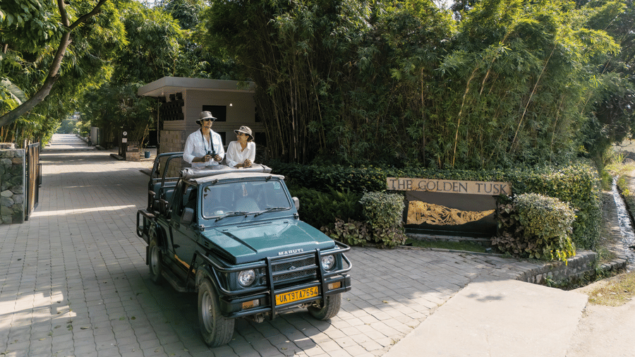 An open vehicle driving along a paved path with people seated inside and greenery on both sides.