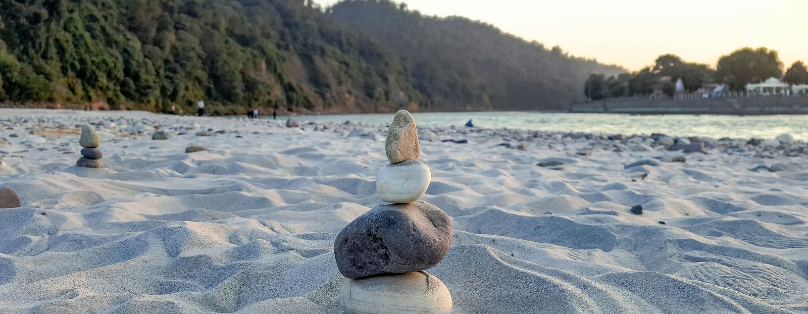An image of pebbles placed on a sandy area with lush green mountains in the background.