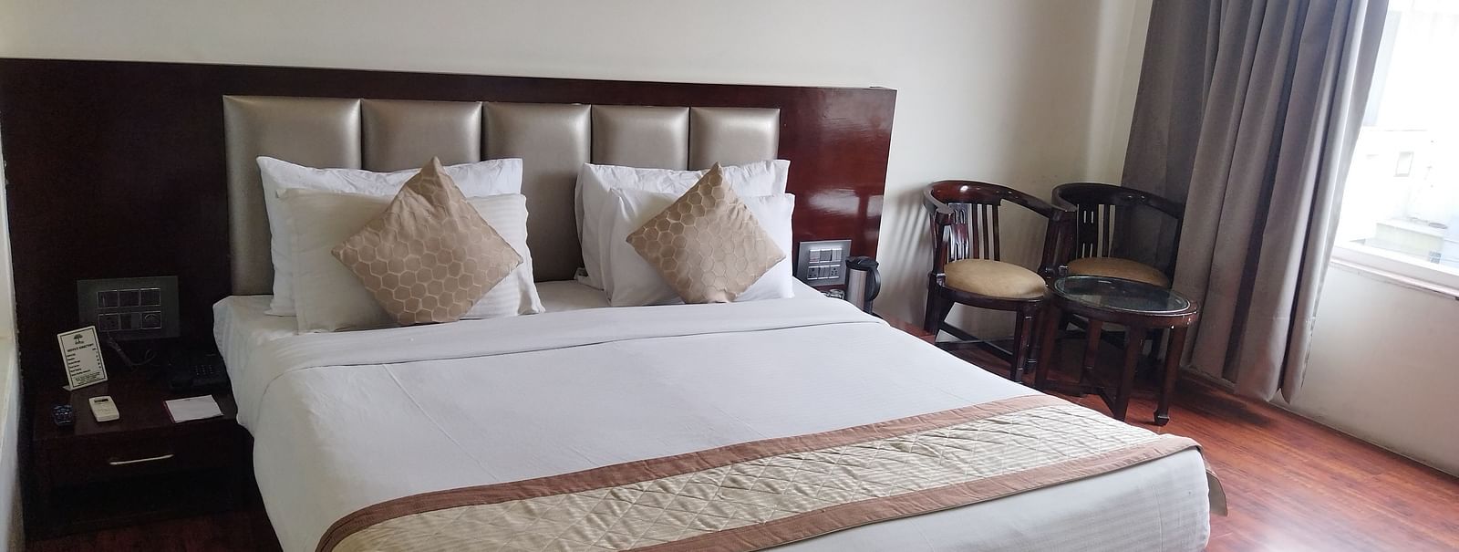 A hotel room with a large bed draped in beige and brown linens and furniture to relax - TGI Apple Inn, Jaipur 