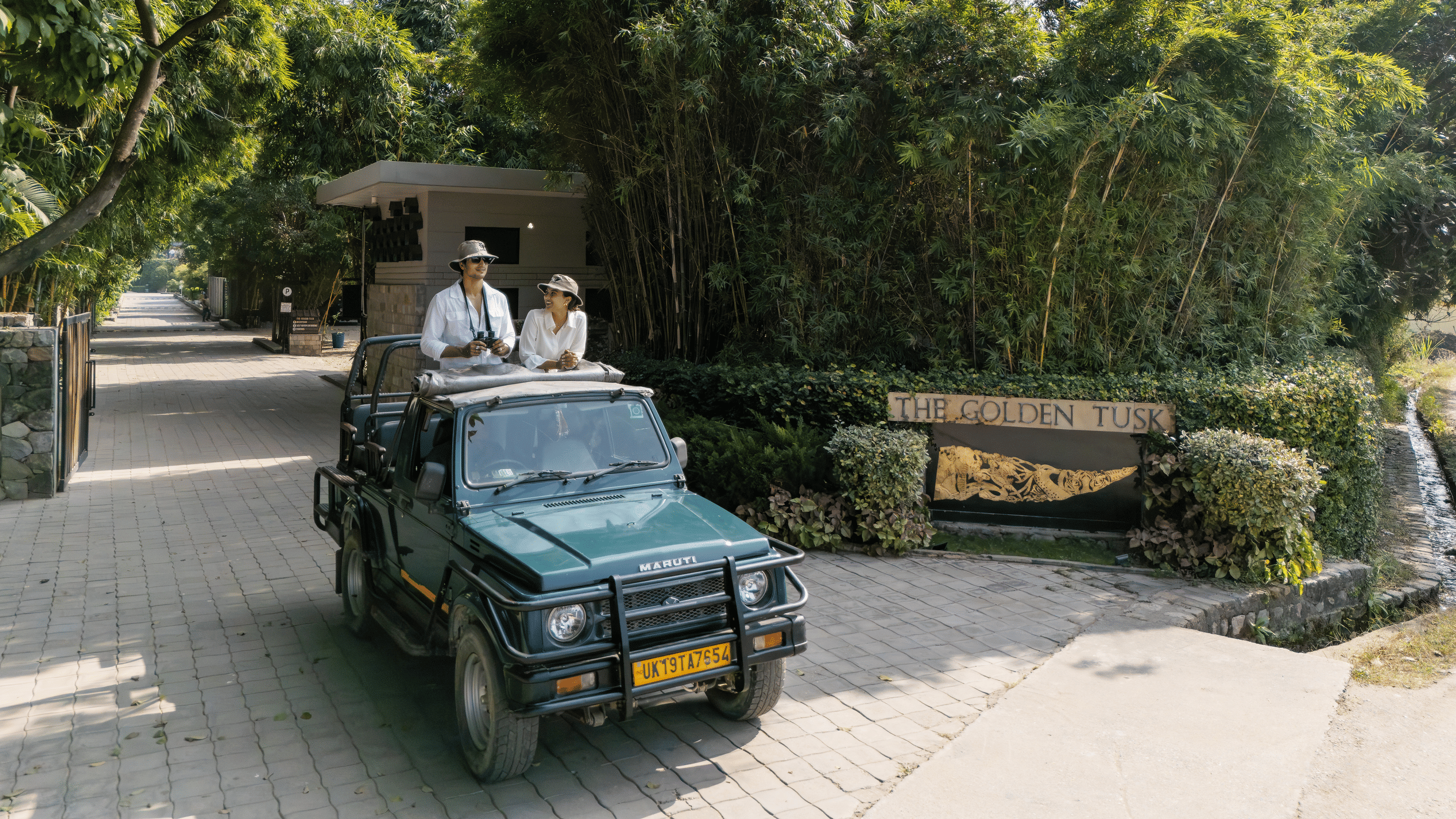 An open vehicle driving along a paved path with people seated inside and greenery on both sides.