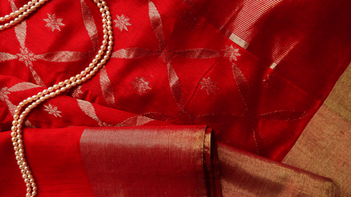 a close up image of a red saree with pearl necklace kept on top of the saree