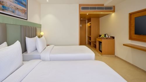 Side view of a room with twin beds and a television in front at Tulip Inn, Bhopal.