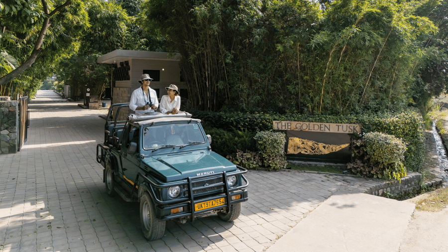 An open vehicle driving along a paved path with people seated inside and greenery on both sides.
