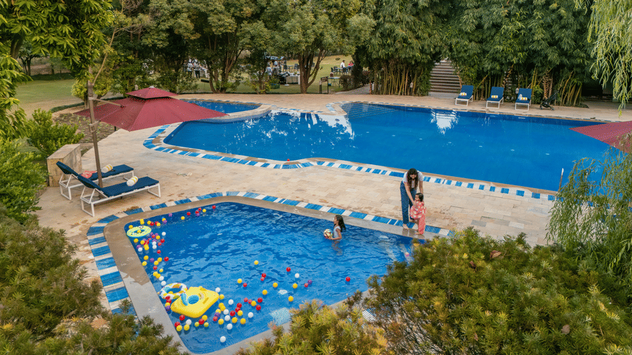 swimming pool with surrounding greenery and buildings in the background at The Golden Tusk, Jim Corbett