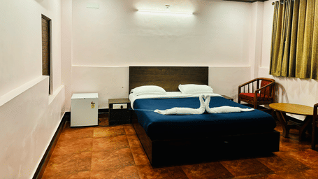 Bedroom with a queen bed, air-conditioning, a wooden table and chairs, a mini fridge and green curtains at Paradise Lagoon Resort, Udupi.