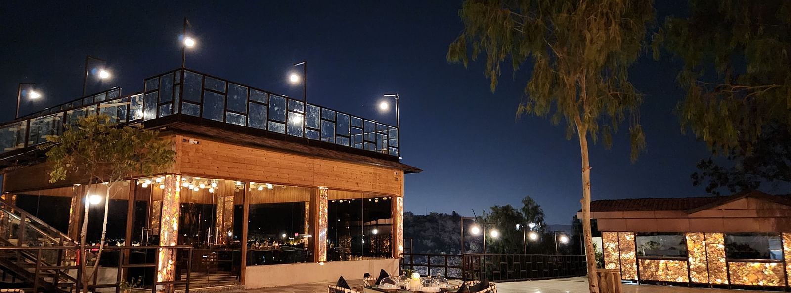An outdoor dining area at night with a table and chairs set on a paved patio. - Bamboo Saa Resort & Spa, Udaipur