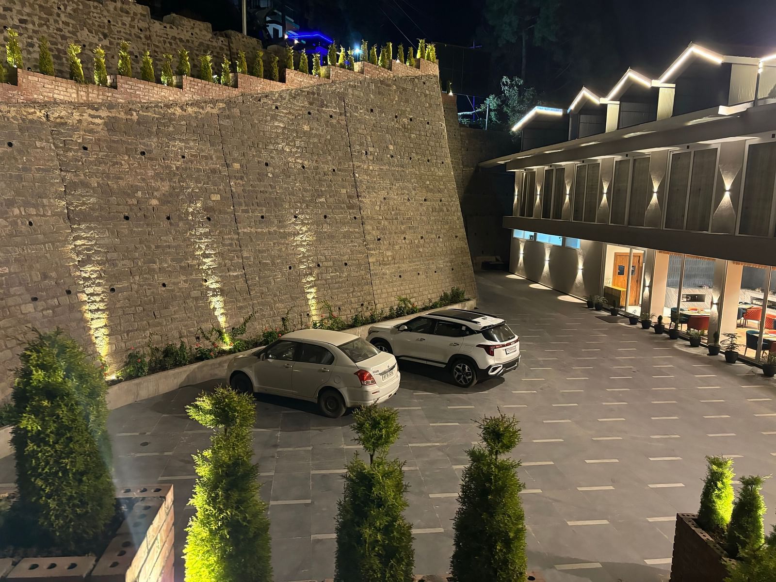 Well-lit outdoor parking area with stone wall and multiple cars parked – ARNISA Boutique Hotel
