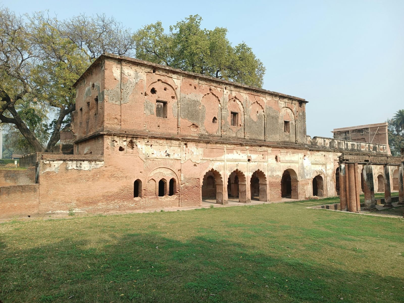 An old red stone building stands against a clear sky, with a trees in the background