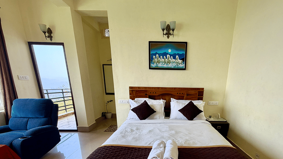 A wooden double bed with white sheets and brown runners, with a blue sofa visible to the left | Kollanoor Guest House, Coorg