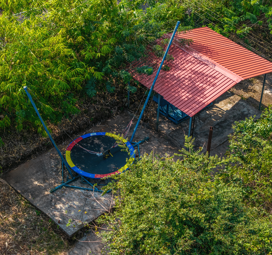 A trampoline and play equipment set up in a garden surrounded by trees.